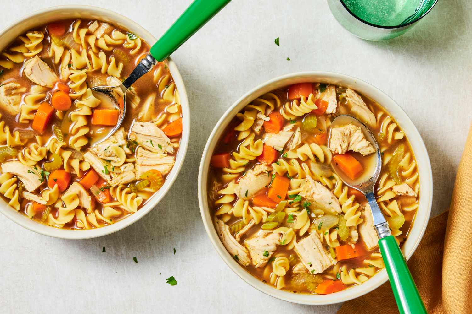 Two bowls of turkey noodle soup with spoons placed on a light table