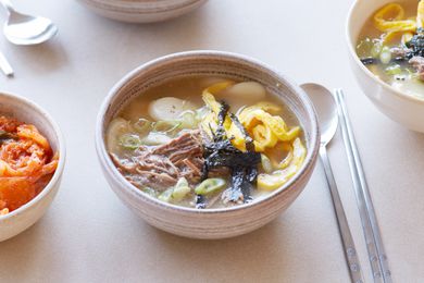 A table set with a bowl of Dduk guk (Korean rice cake soup) and spoons.