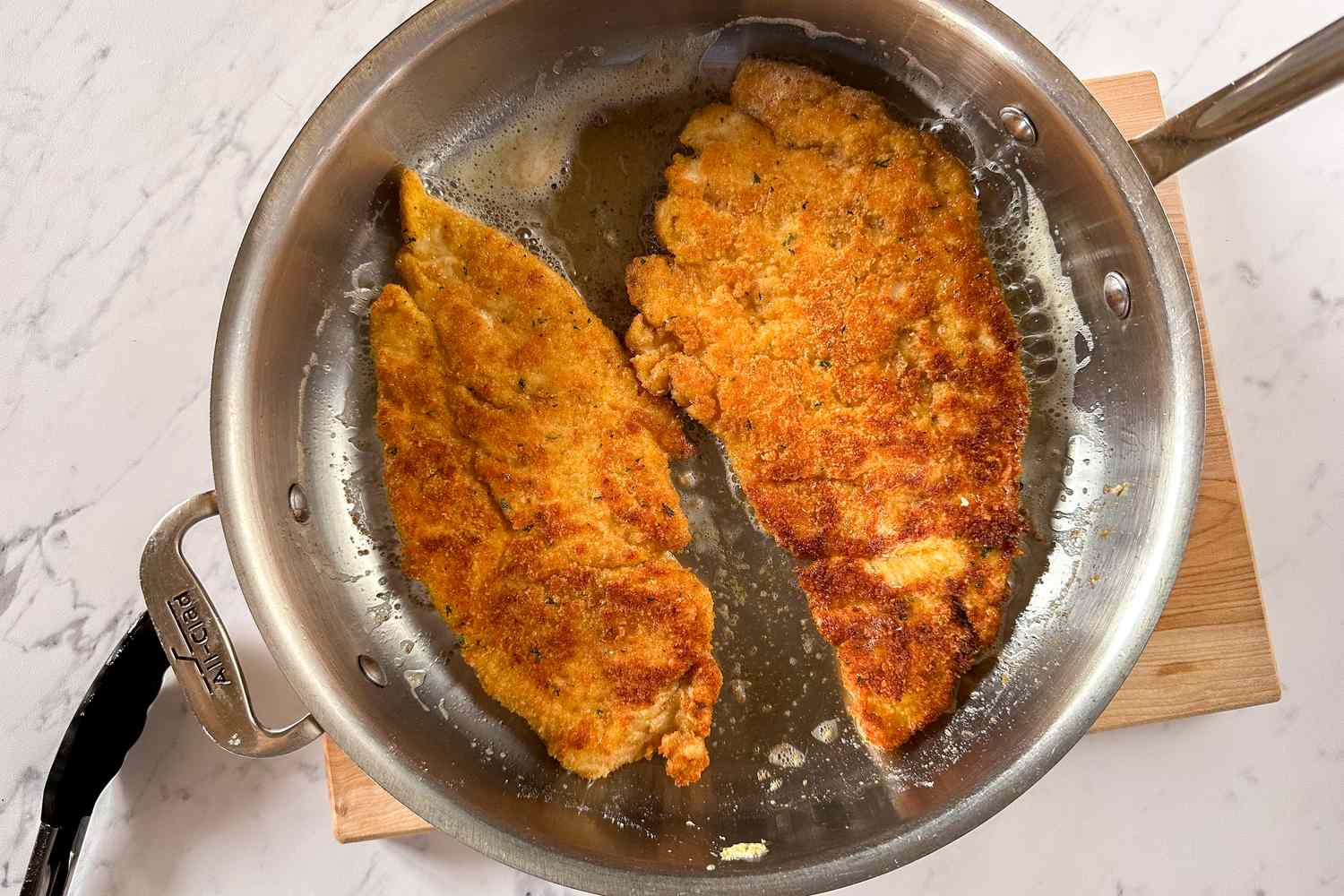 Overhead shot of two breaded chicken cutlets getting panfried