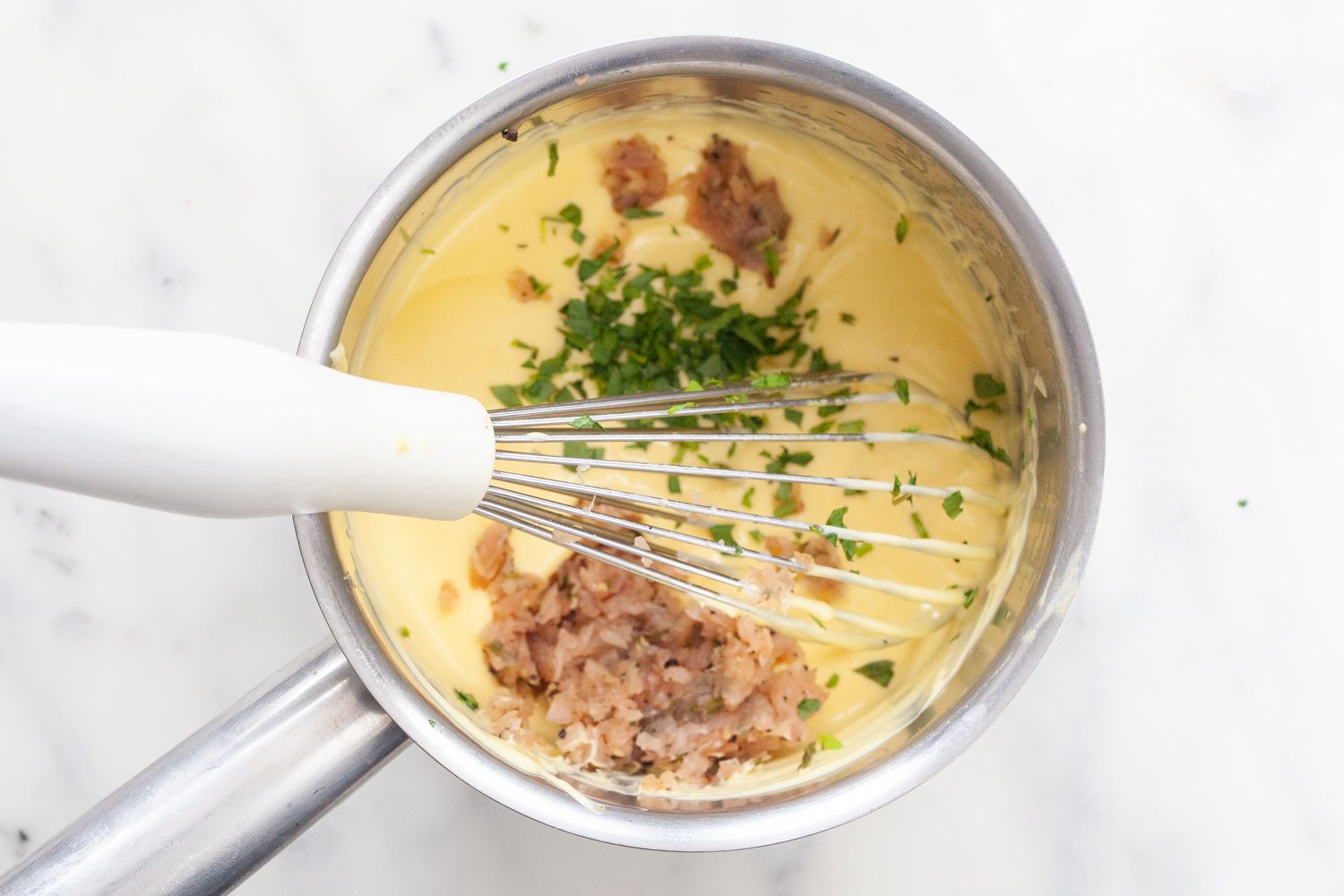 Adding shallots and tarragon to a sauce pan with thickened béarnaise sauce.
