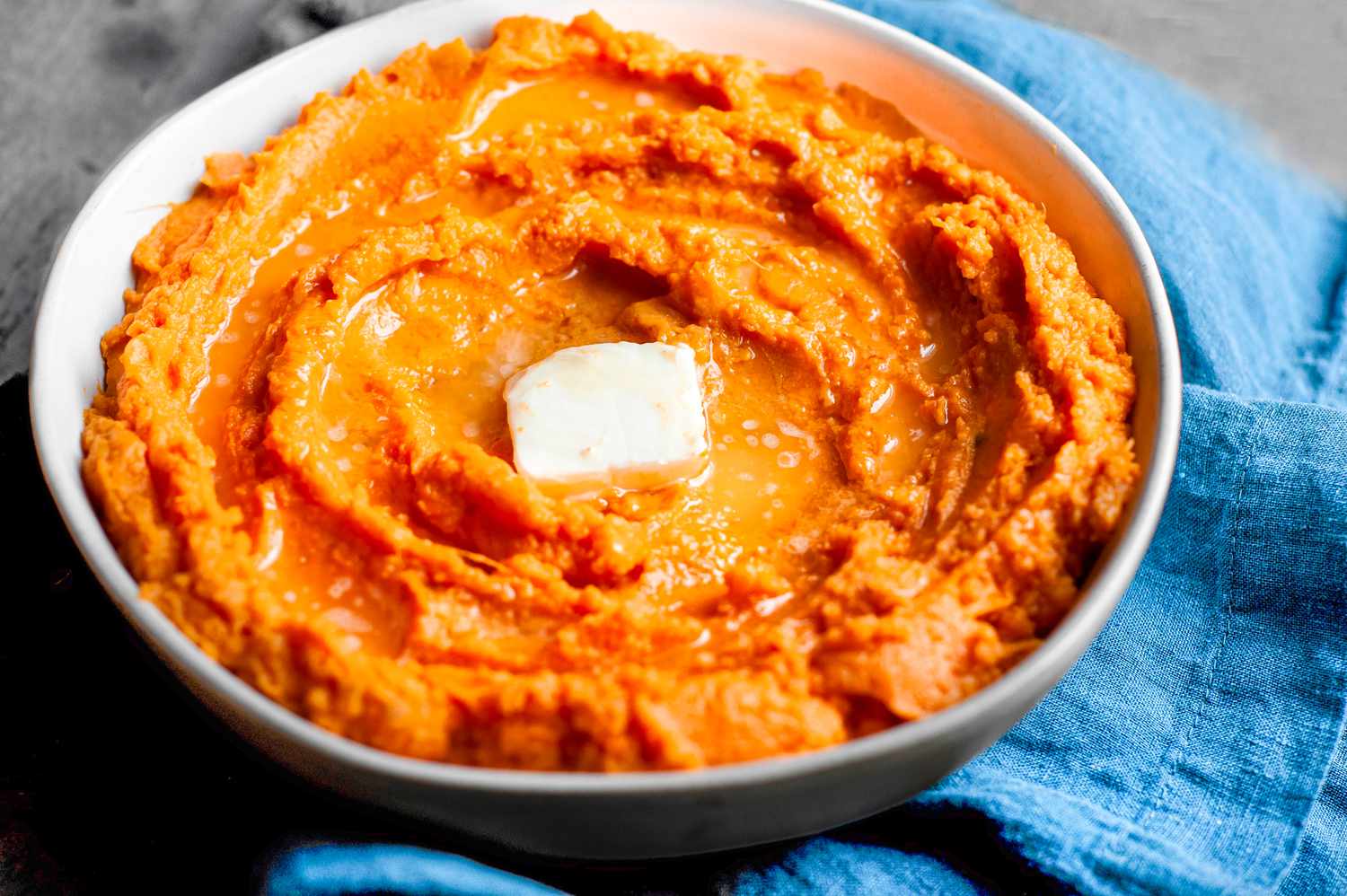 Bowl of Instant Pot Mashed Sweet Potatoes Topped with Butter on a Table Napkin