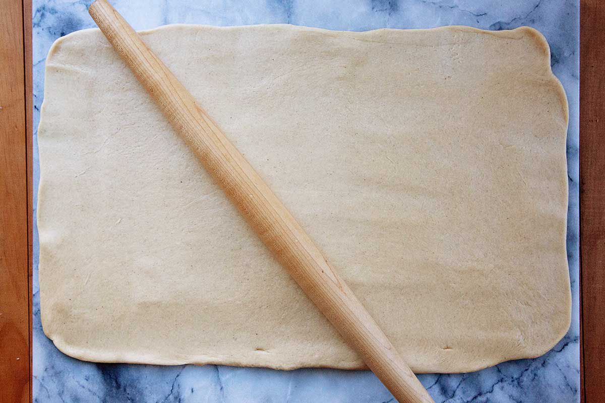Easy king cake dough is rolled into a large rectangle. A rolling pin is resting on top.
