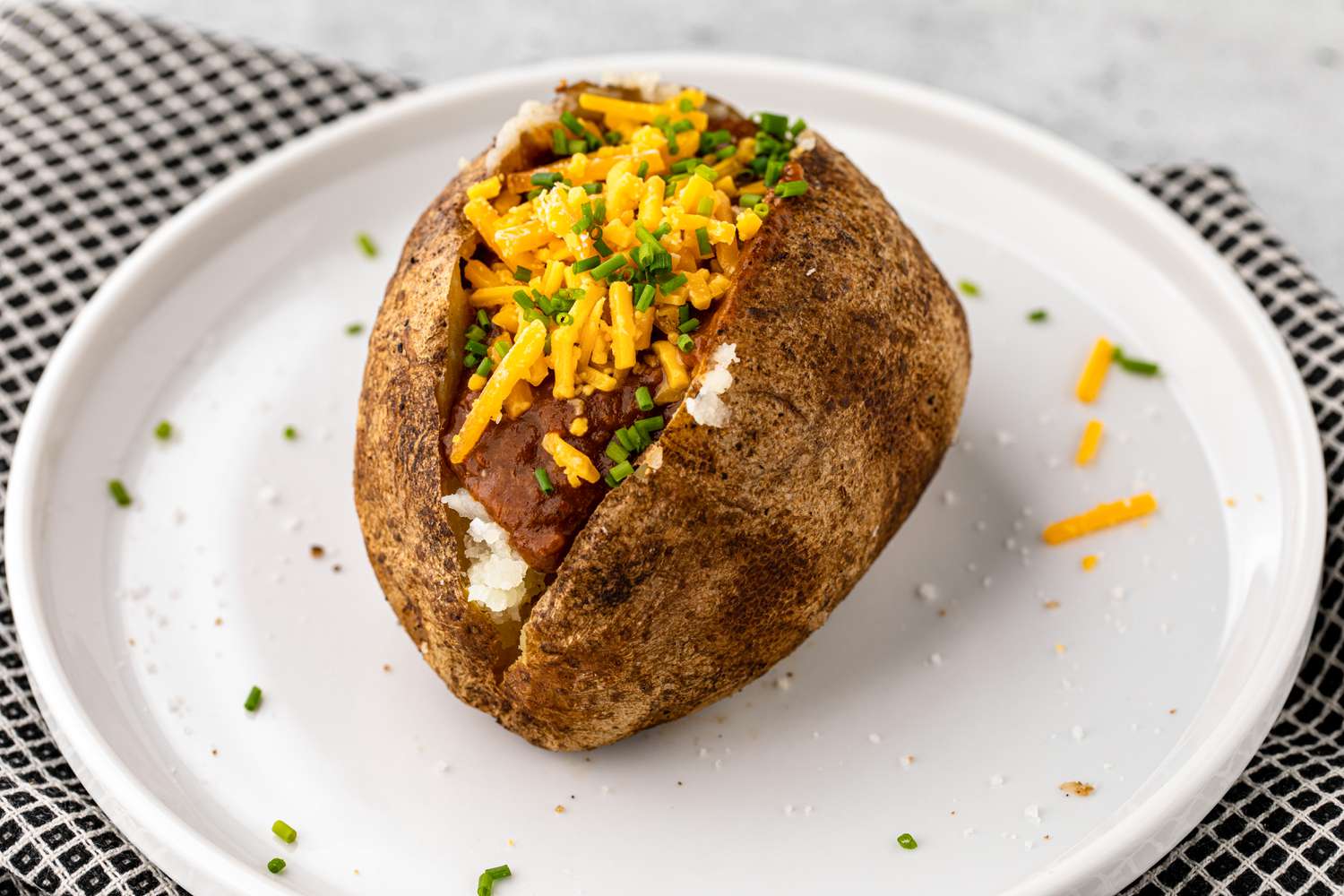 Grilled Baked Potato Topped with Chili, Cheese, and Chives on a Plate 