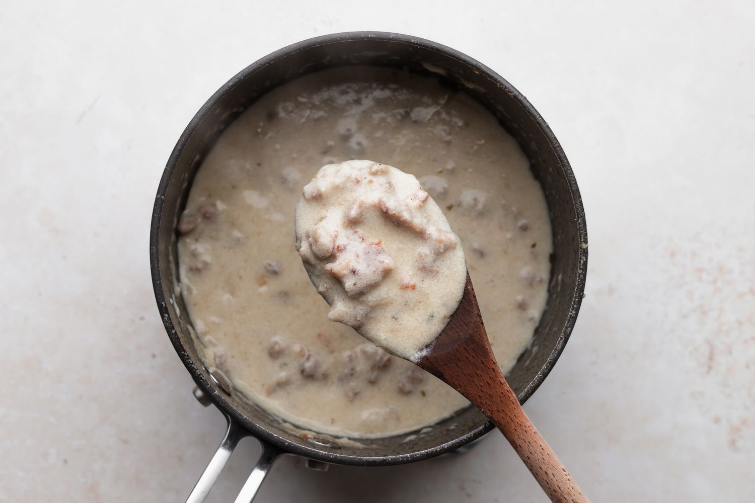 Sausage gravy in a pot with a wooden spoon for biscuits and gravy.