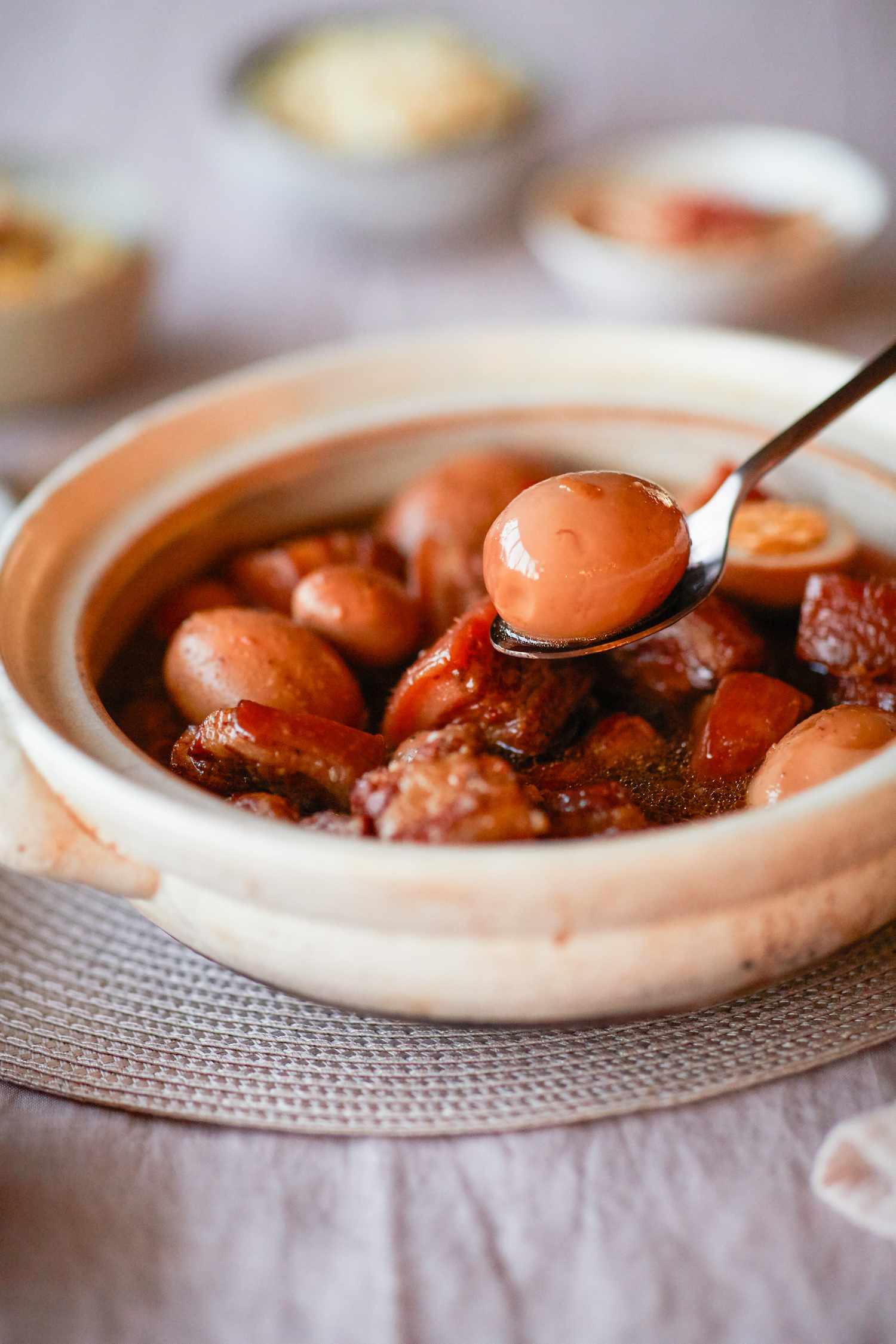 A bowl of Vietnamese braised pork belly and eggs and a spoon lifting some out of the bowl.