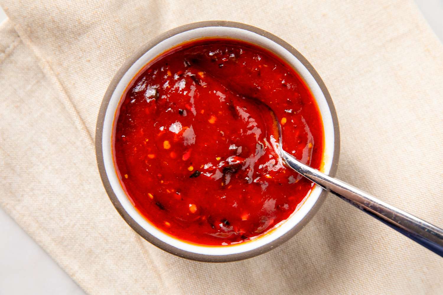 A small bowl filled with sweet and sour sauce, accompanied by a spoon resting on the edge of the bowl