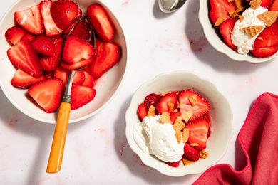 Strawberry dessert bowls with toppings like whipped cream and crushed cookies on a white background