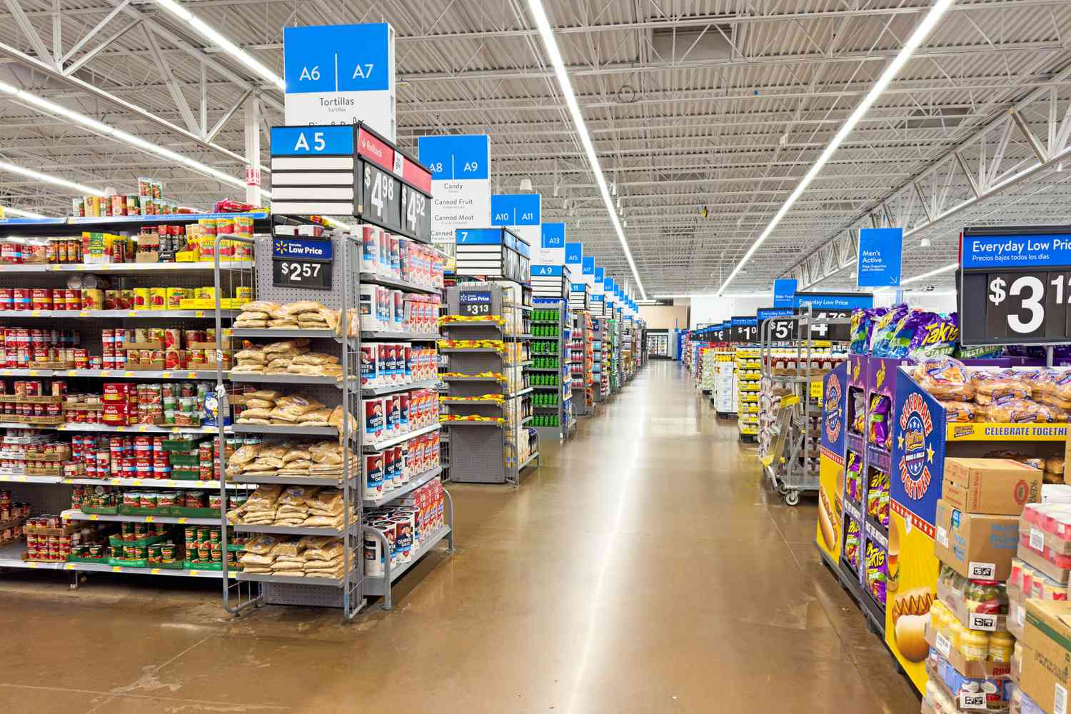 A Walmart supermarket aisle with shelves stocked with various grocery items and overhead section signs visible