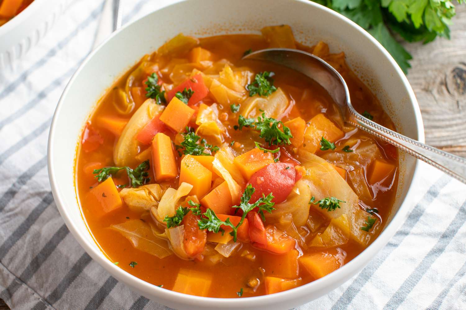 Healthy vegetarian and detox soup with fresh vegetables and cabbage. Served in a bowl with spoon on wooden table