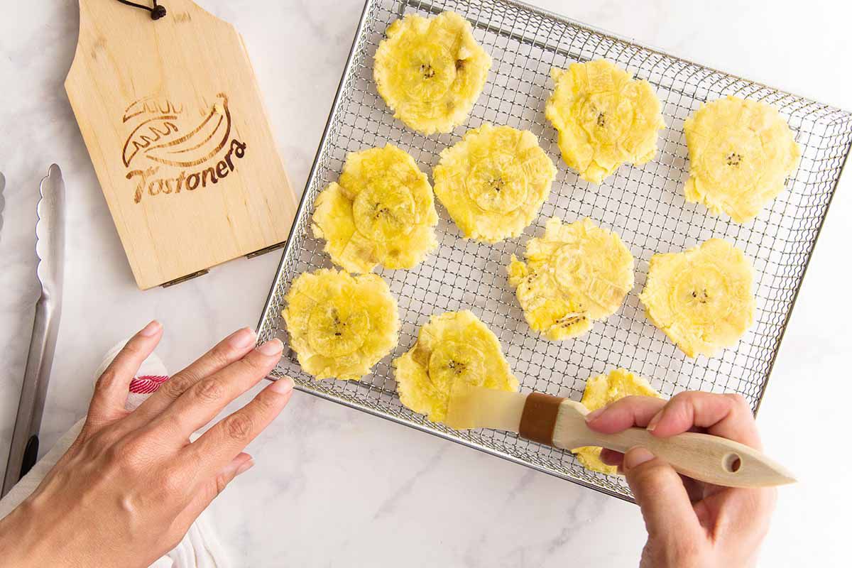 Brushing smashed plantains aka Tostoneswith oil