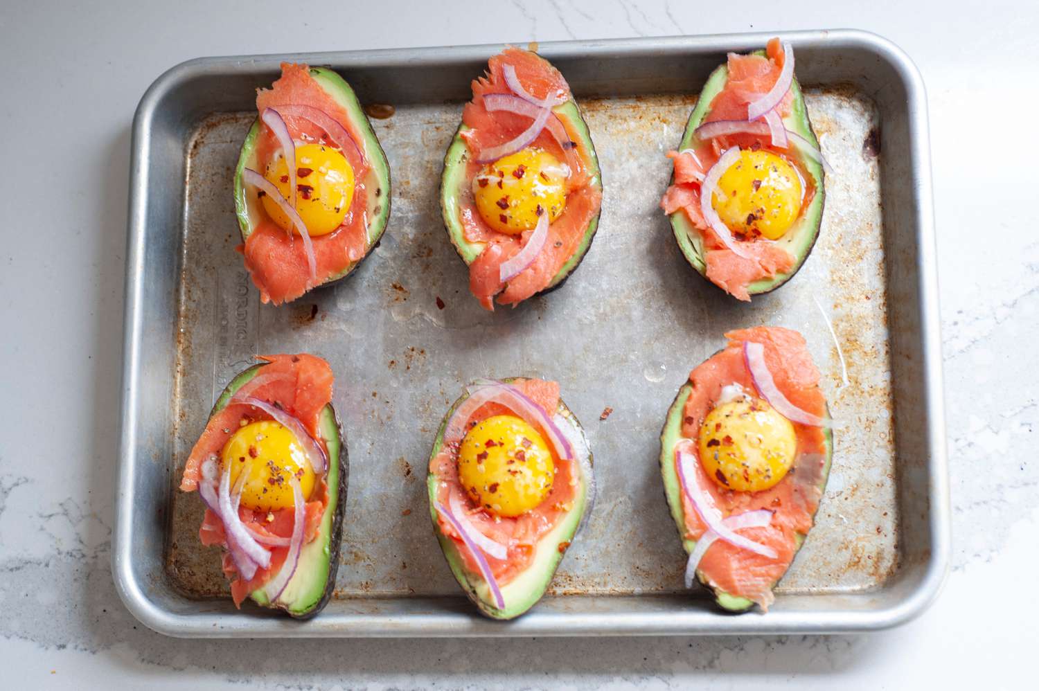 Baked eggs in avocado with everything bagel seasoning on a sheet pan and ready to be baked.
