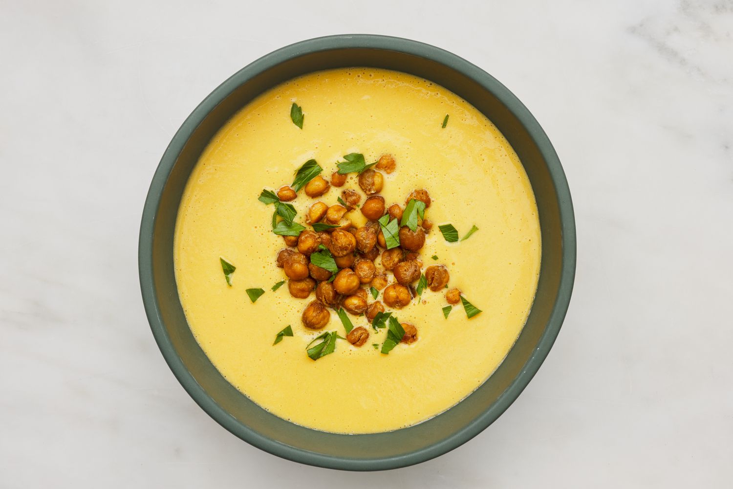 Bowl of hummus soup topped with roasted chickpeas and chopped flat parsley