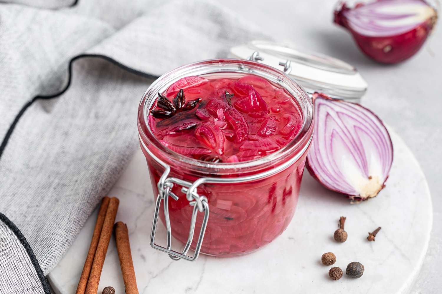 A jar of refrigerator pickled onions on a linen with sliced red onion next to it.