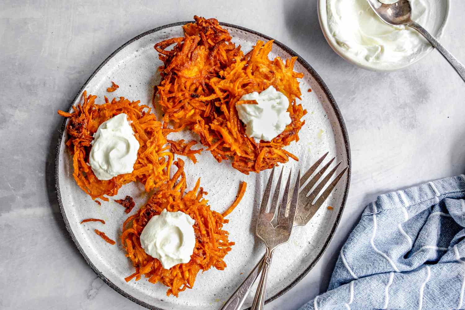 Plate of Sweet Potato Latkes Topped with Dollops of Sour Cream and Next to It, a Small Bowl with More Sour Cream