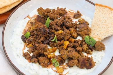 Dish featuring spiced ground meat over a creamy yogurt mixture garnished with mint leaves and served with flatbread