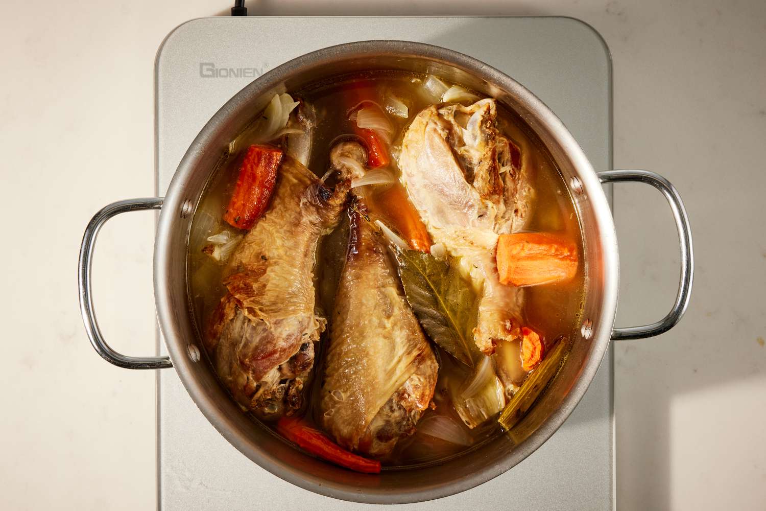Overhead view of a metal pot on a hot plate with turkey legs, carrots, celery, onions, broth and spices for Best Ever Gravy recipe