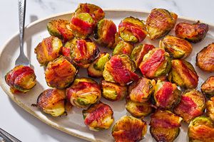 Closeup of bacon wrapped Brussels sprouts on a large oval serving plate, with a fork stuck into one of the sprouts