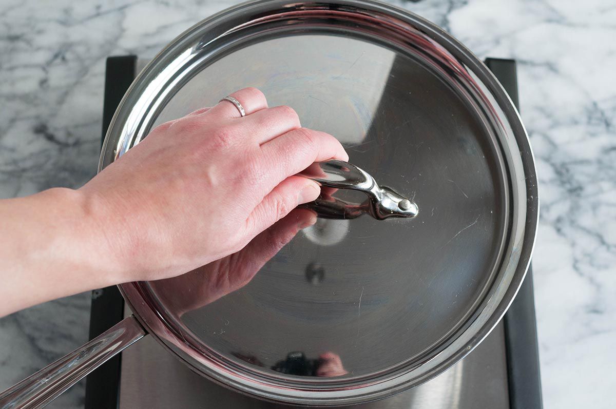 A hand placing a lid on a saucepan