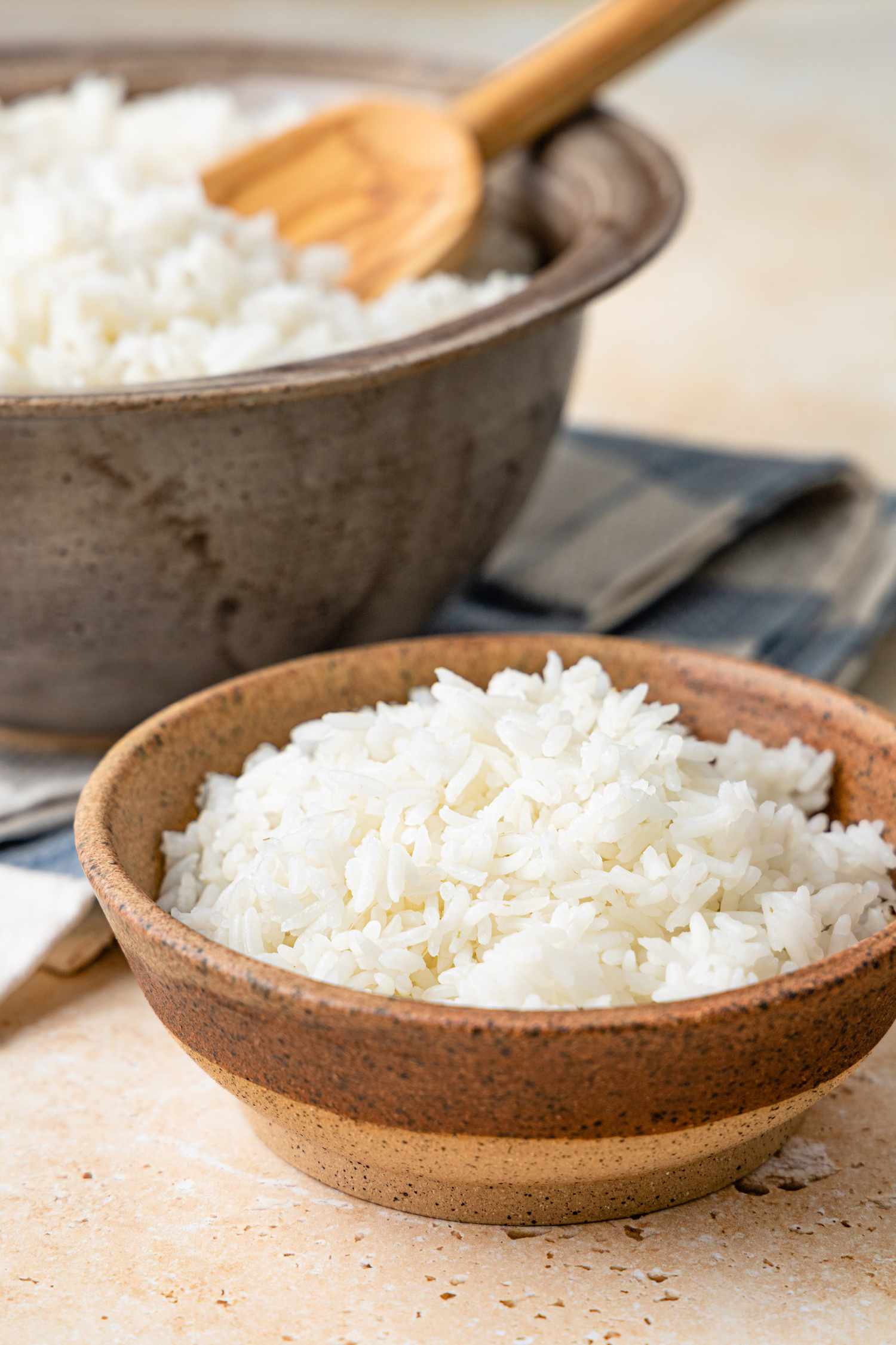 Small Bowl of Microwave Rice, and in the Background, a Larger Bowl with a Wooden Spoon in It 