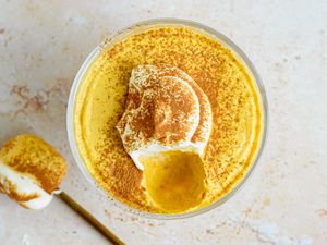 Overhead shot: 2-ingredient pumpkin mousse topped with whipped cream and a sprinkle of pumpkin spice, all in a sherbert glass. On the counter, a spoonful of mousse