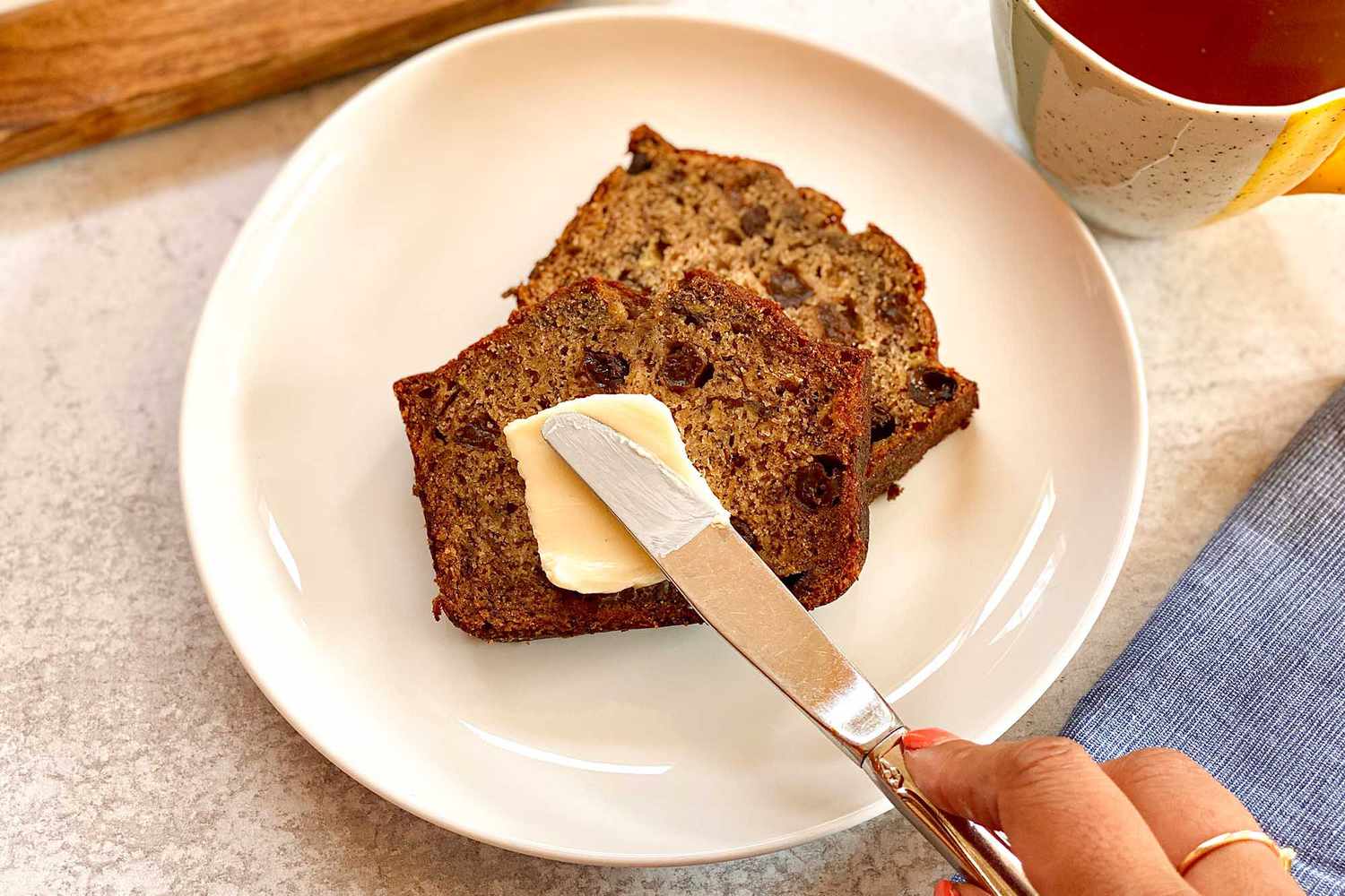 Two slices of rum raisin banana bread on a plate and getting butter spread on top.