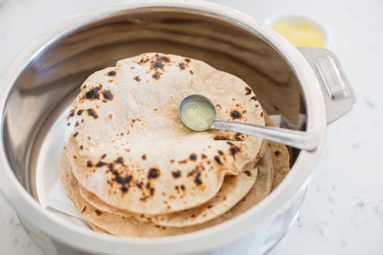 A stack of roti in a large pot with a small ladle of ghee on top of it.