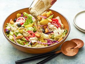 Salad Dressing Poured Over a Bowl of Olive Garden Salad, and on the Counter Next to It, a Stack of Plates and a Set of Salad Serving Utensils