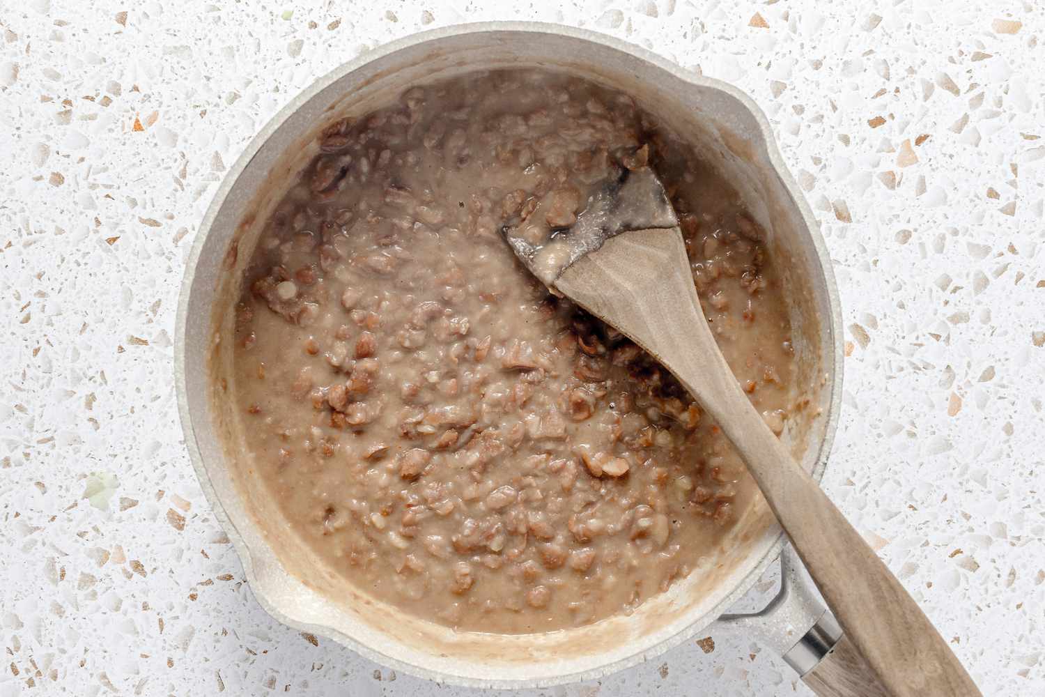 Cooked, Mashed Beans in a Dutch Oven With a Wooden Spoon for Easy Rice and Beans Freezer Burritos Recipe