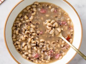 A bowl of cooked blackeyed peas in broth with pieces of meat and a spoon