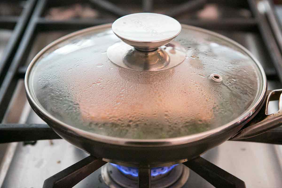 Salmon poaching in a pan with a lid on a gas stove