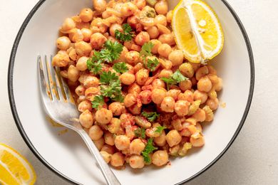 A plate of cooked chickpeas garnished with parsley and paprika, served with lemon wedges and a fork