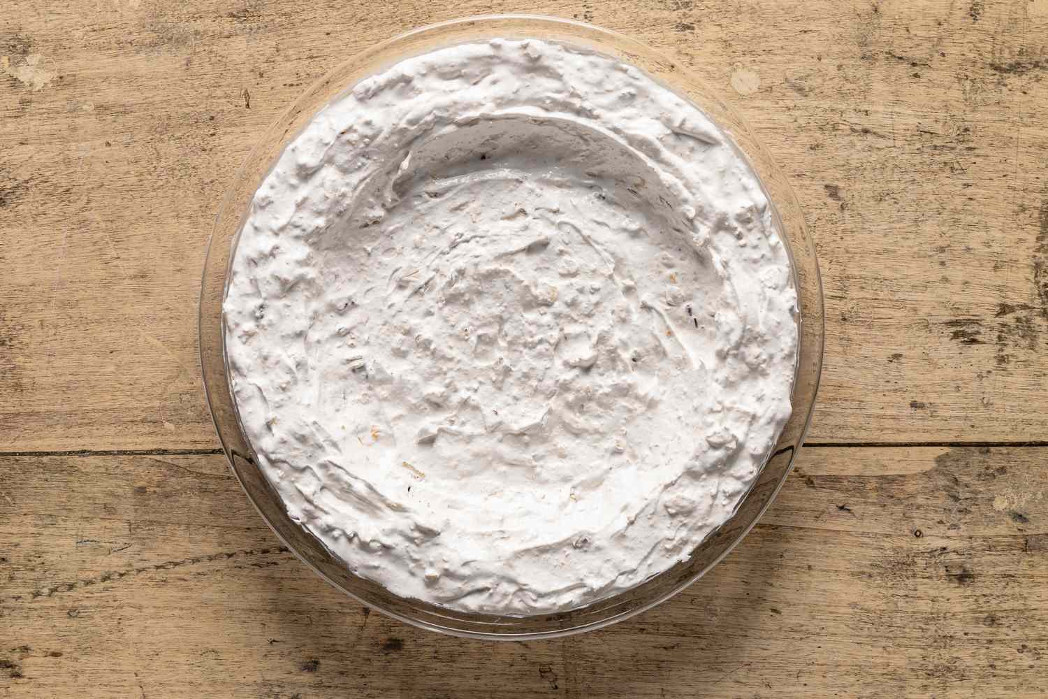 Overhead view of a clear glass pie plate after folding in the saltine crackers, pecans, and vanilla into the egg white mixture then forming to plate for Company's Coming Pie recipe
