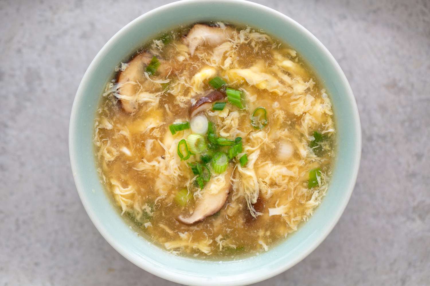 An overhead of a Bowl of egg drop soup with mushrooms and spring onions