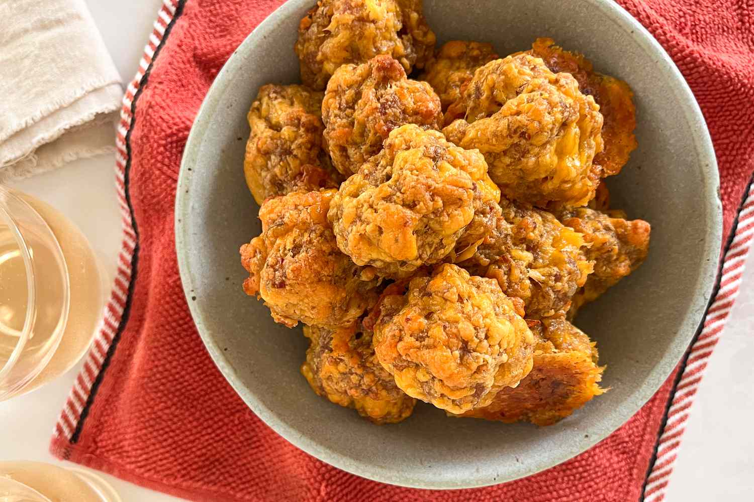 Overhead view of a green bowl of sausage balls resting on a red towel on a white countertop