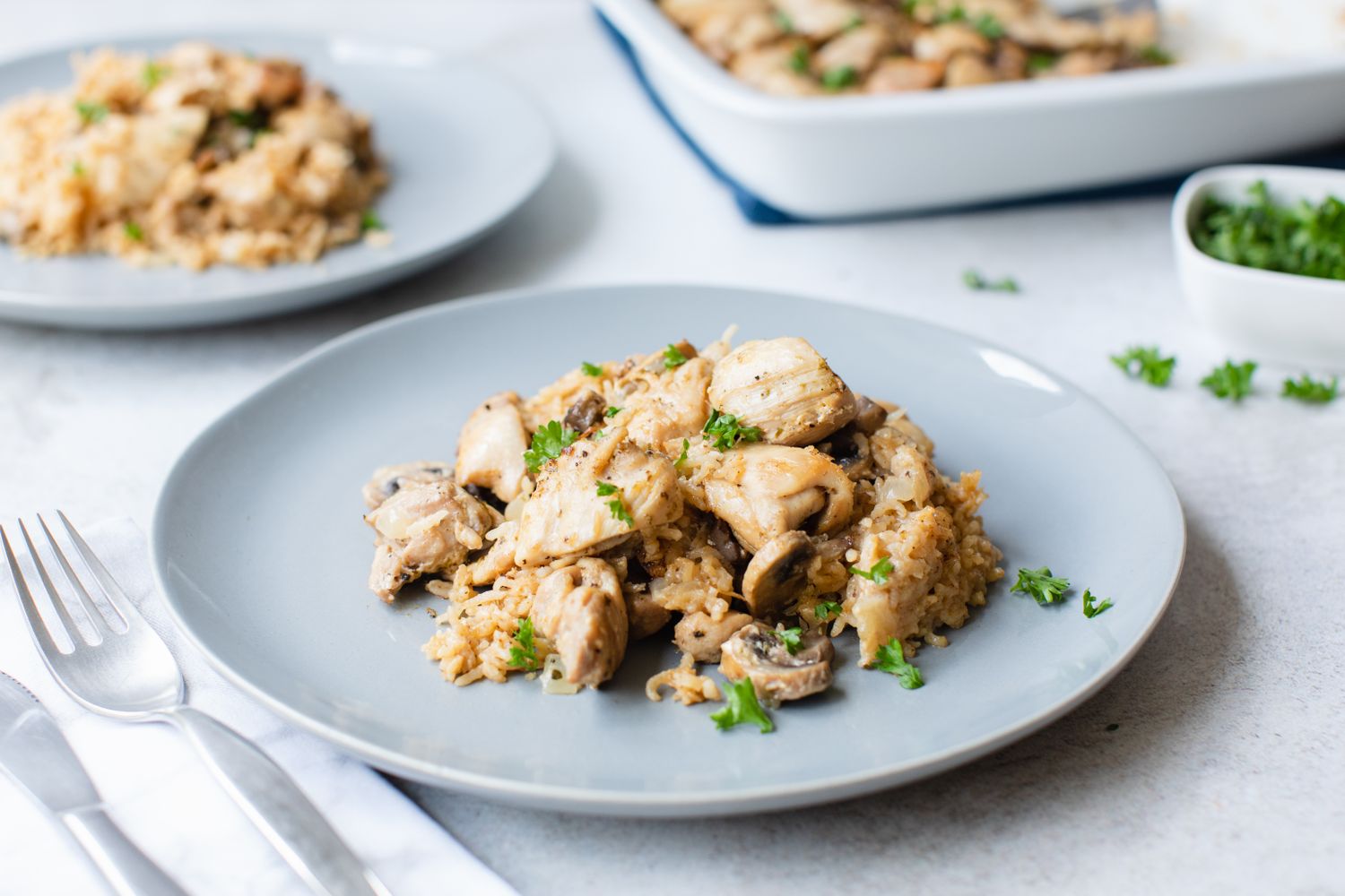 A plate of chicken and rice casserole garnished with parsley served on a table with cutlery nearby