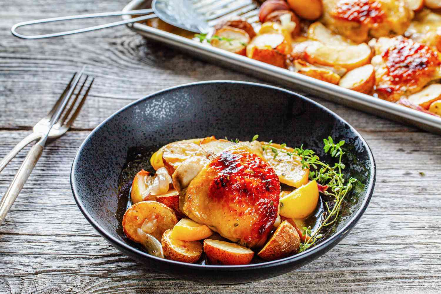 Bowl of Sheet Pan Honey Roasted Chicken Thighs with Baby Potatoes, Apples, Shallots, and Thyme with the Rest in the Background