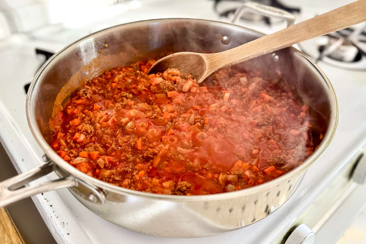 A pot of bolognese sauce on a stove with a wooden spoon