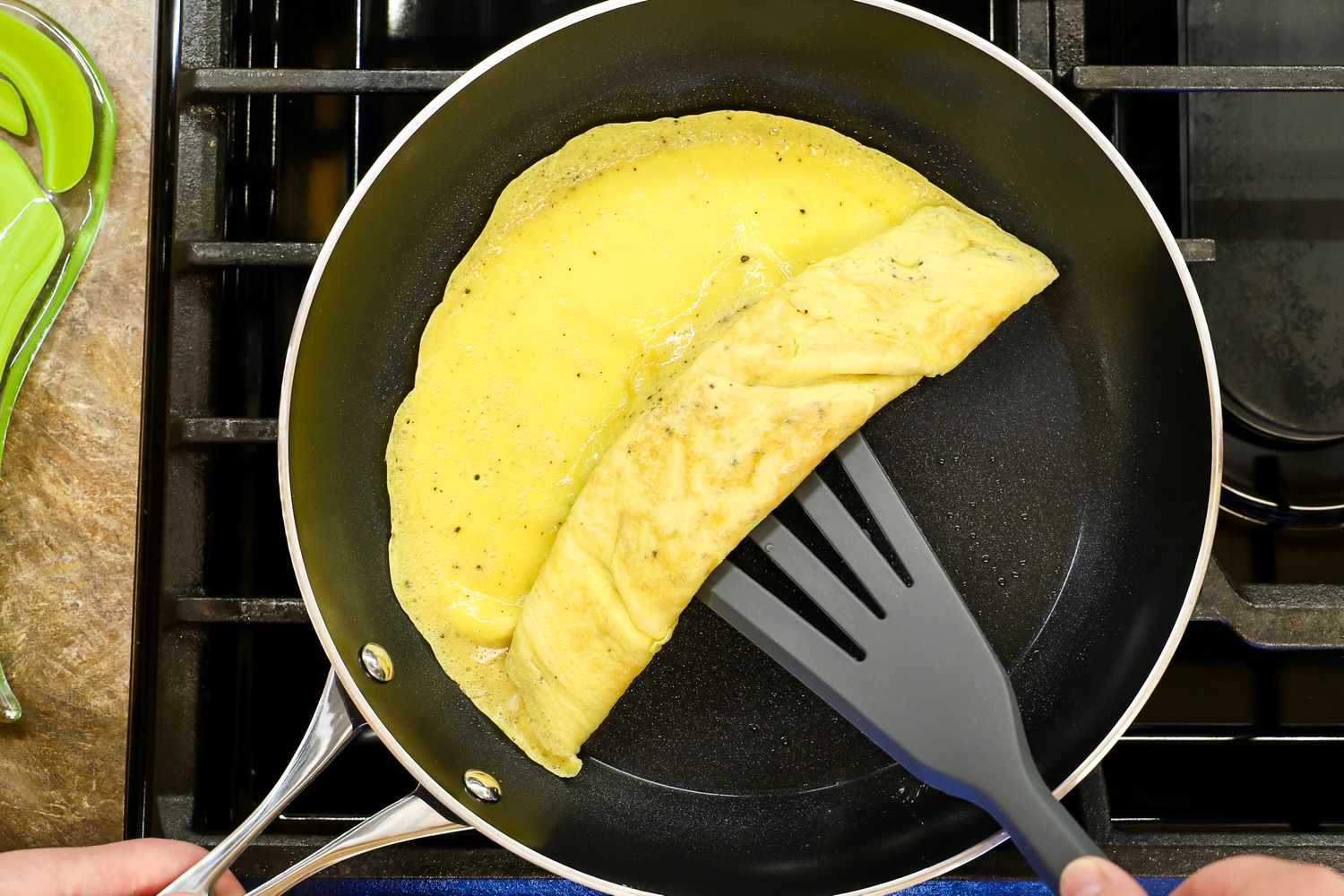 A spatula folding an omelet in a Kyocera ceramic pan on a stovetop
