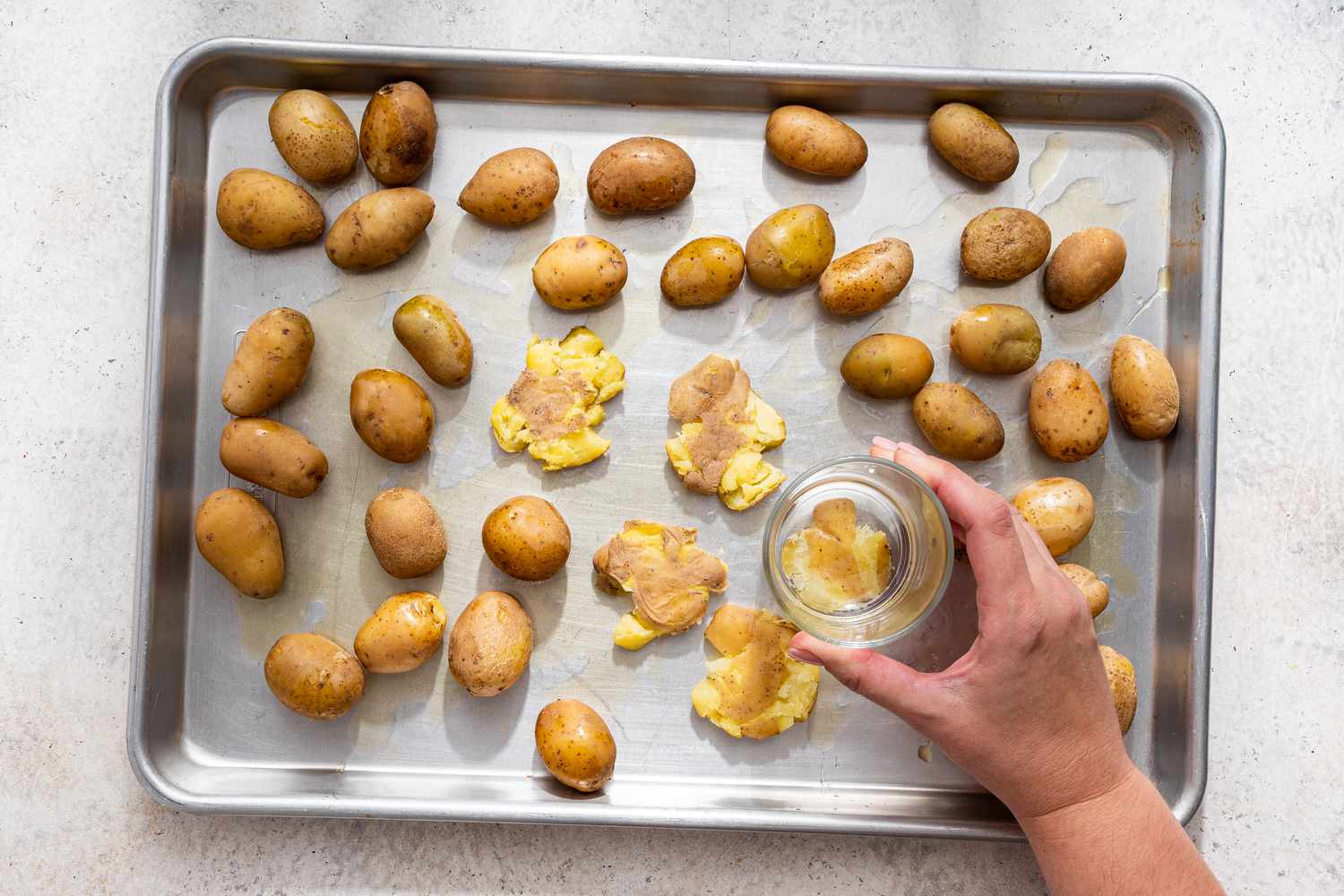 Boiled potatoes flattened on the baking sheet using the bottom of a glass for Australian crash hot potatoes recipe