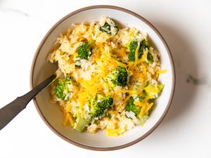 A bowl of rice mixed with broccoli and topped with melted cheese a spoon on the side