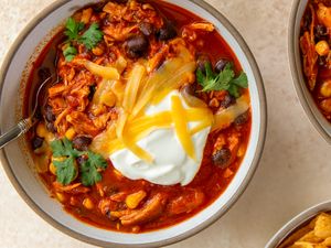 Bowl of chili with shredded chicken topped with sour cream and cheese and garnished with cilantro