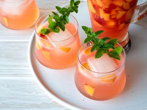 Two Glasses of Ginger Peach Rum Punch Garnished with Mint Next to a Pitcher