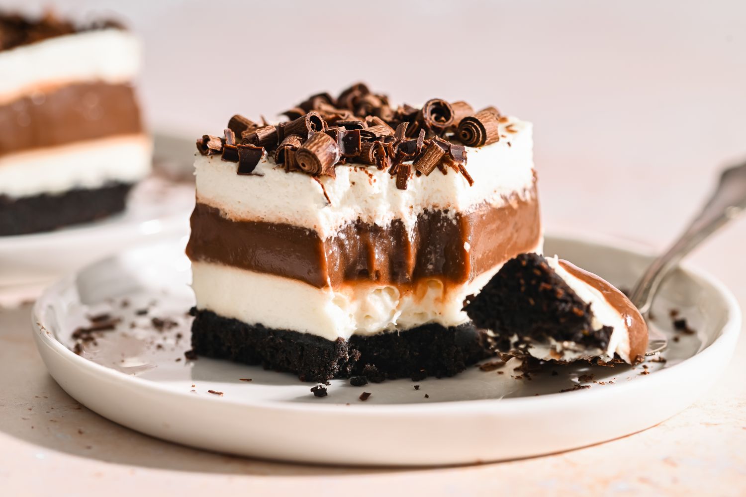 A layered chocolate dessert topped with chocolate curls on a plate a fork beside it