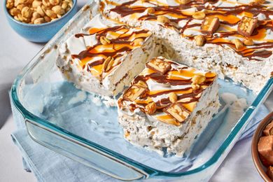A dessert in a glass baking dish, topped with peanuts, caramel, chocolate drizzle, and candy pieces