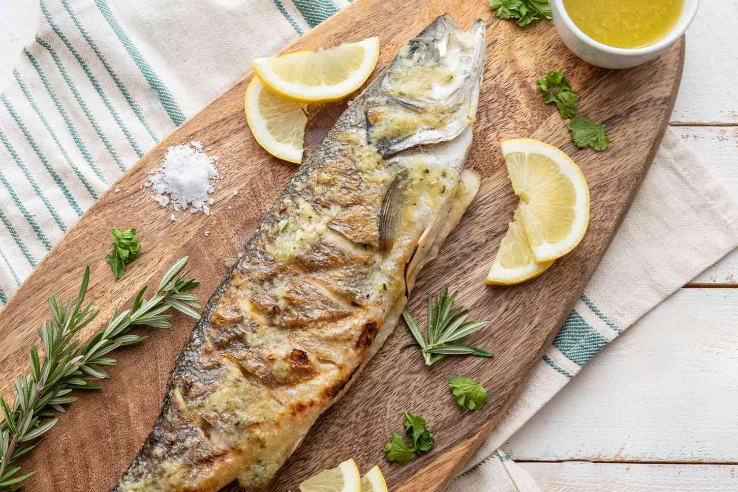 Overhead view of a whole branzino fish on a platter with lemon wedges and herbs.