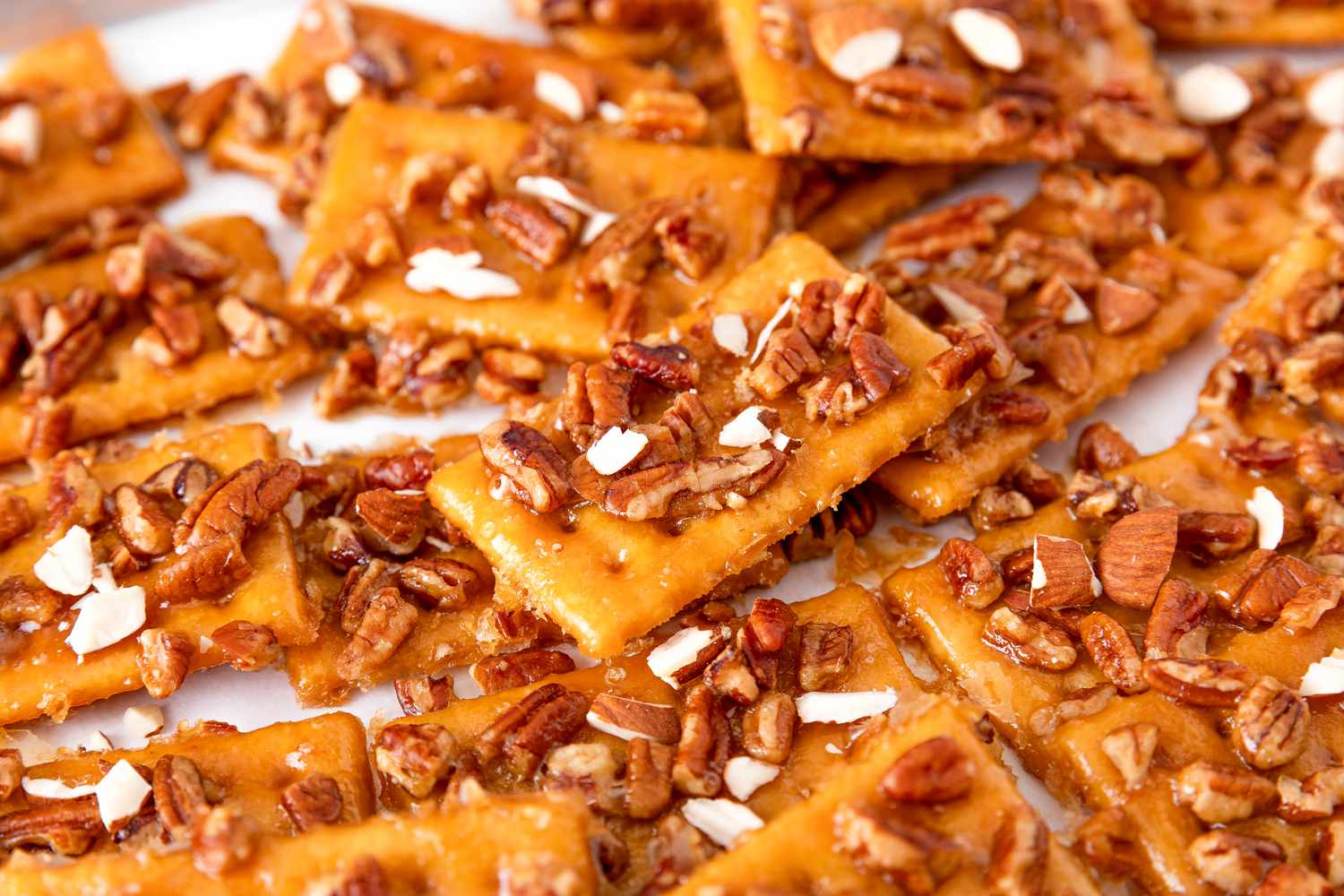 Closeup of club cracker cookies topped with chopped mixed nuts spread out on a white surface