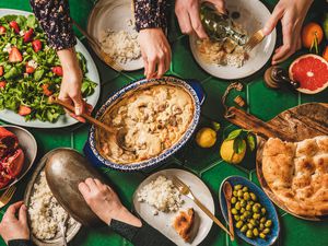 Family having Turkish dinner. Flat-lay of hands serving and eating with lamb in yogurt sauce, fresh arugula and strawberry salad, rice pilaf and flatbread.