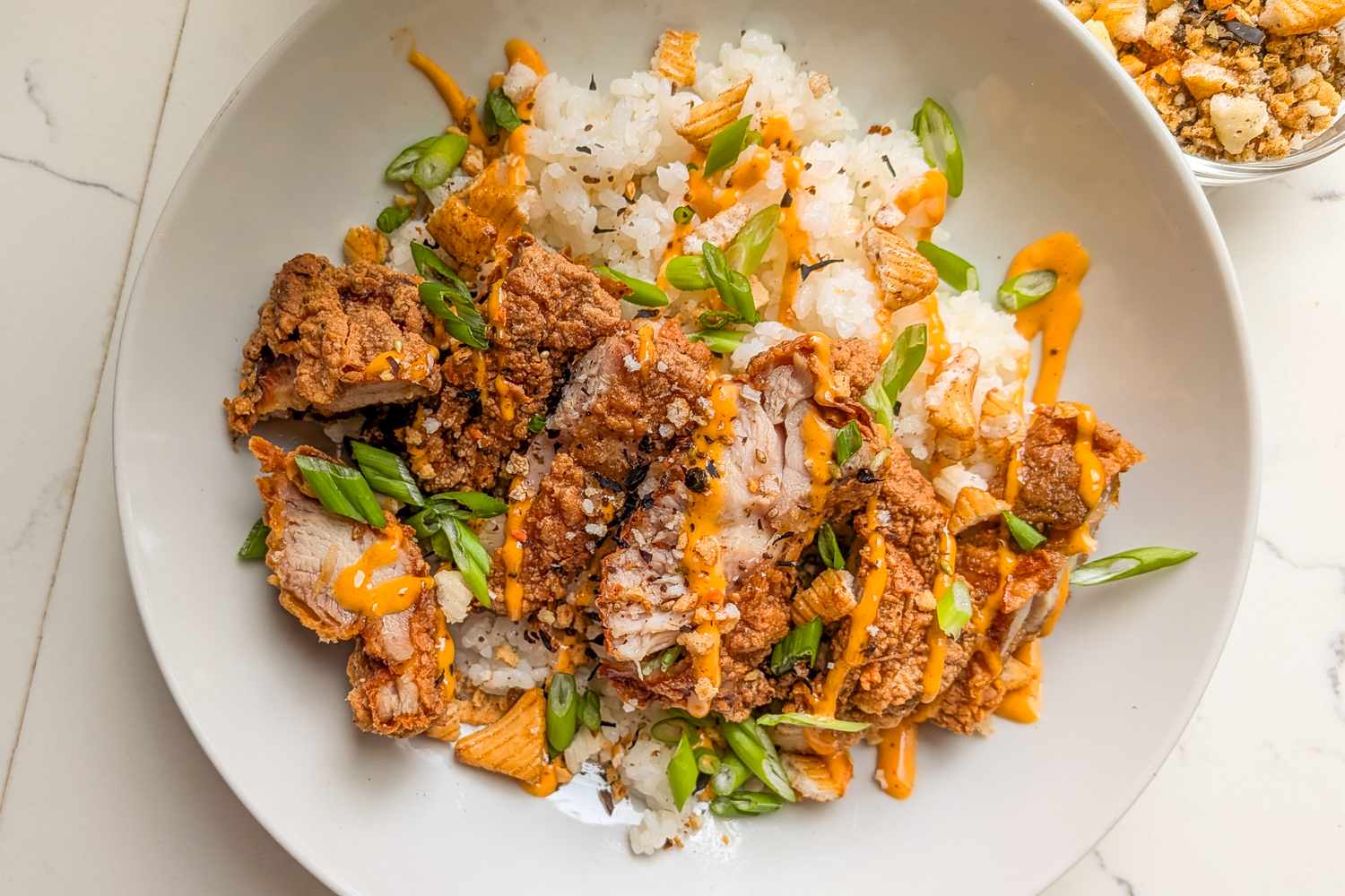A plate of mochiko chicken served with rice garnished with green onions and sauce