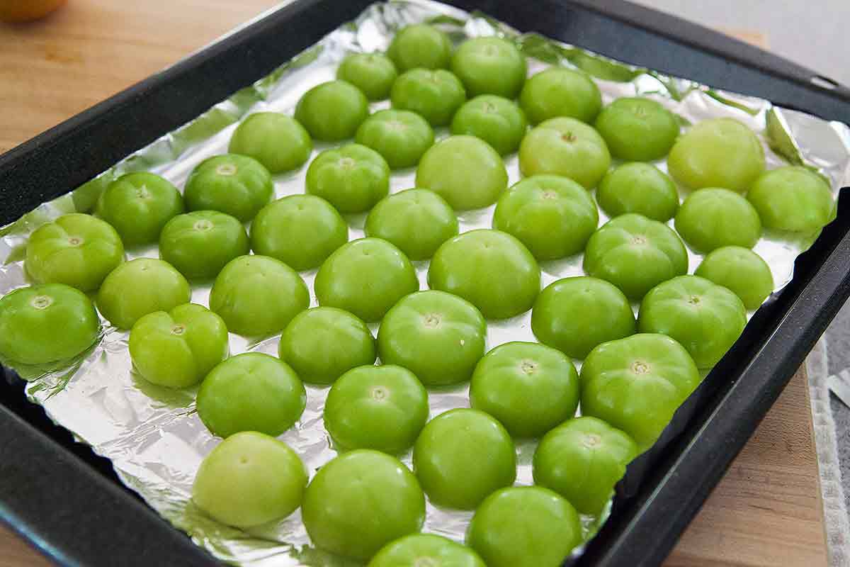Tomatillos cut in half and resting, cut side down, on a foiled baking sheet