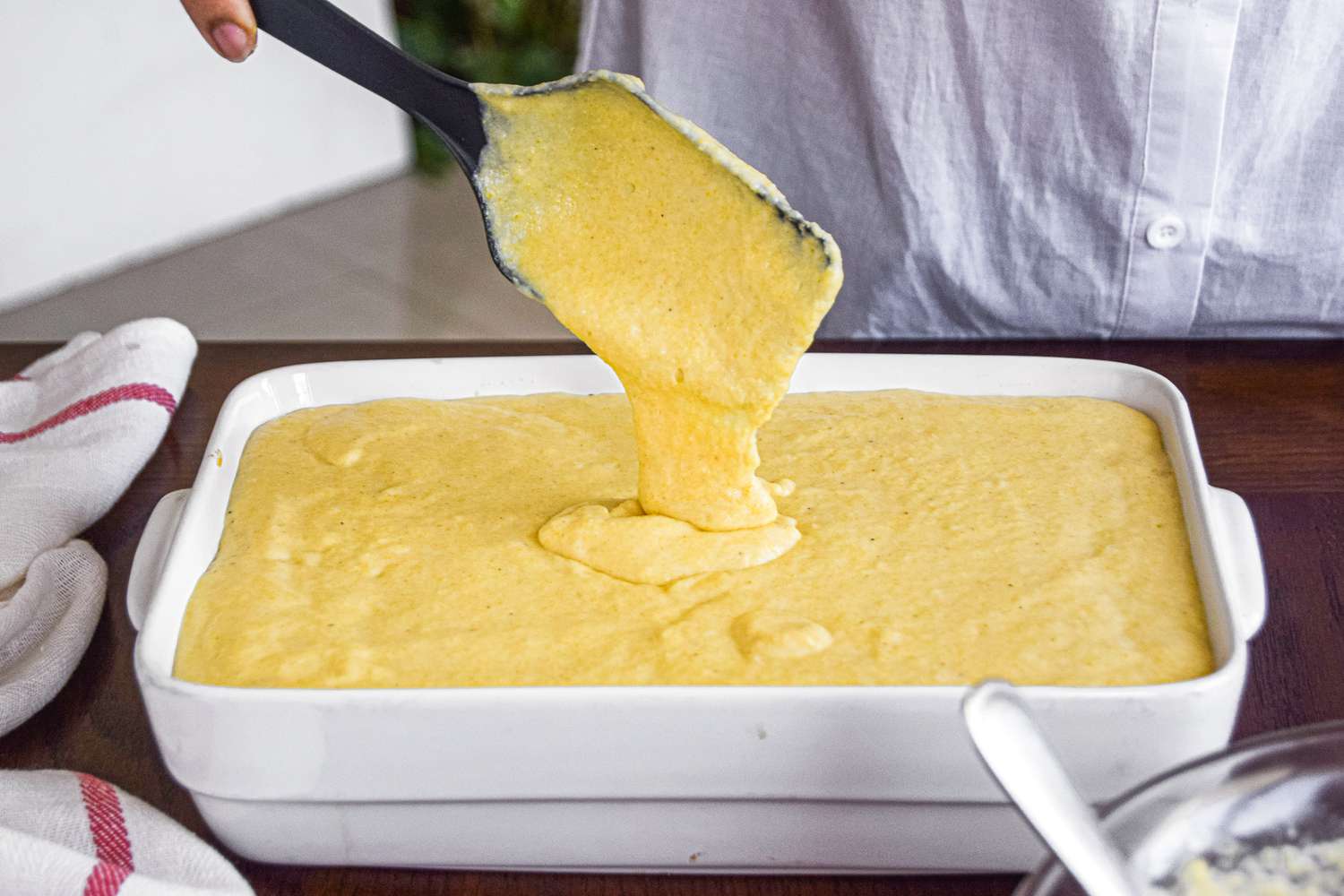 Spooning the cornmeal topping over the filling to make a tamale pie recipe.